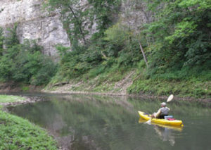 paddling a kayak on a small river with limestone bluffs
