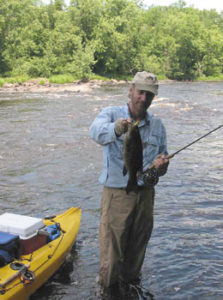 Tim Holschlag wade fishing beside his kayak, holding a big smallie