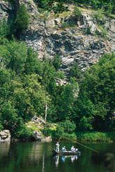 Anglers fly fishing in front of tall limestone bluffs and forest