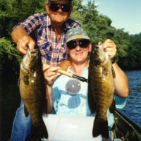 An angler and his father in the boat, each holding a big smallmouth bass.